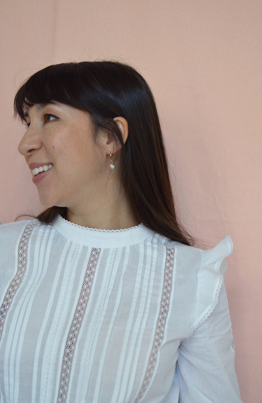 The upper body of Nina, a dark haired woman, wearing a white blouse with tucks and lace inserts