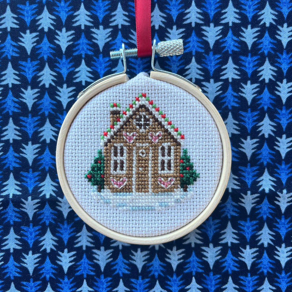 Gingerbread House cross stitch ornament on a blue Christmas tree print fabric